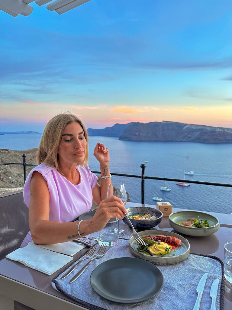 dove alloggiare a Santorini - tavola con piatti e ragazza vista mare a Santorini