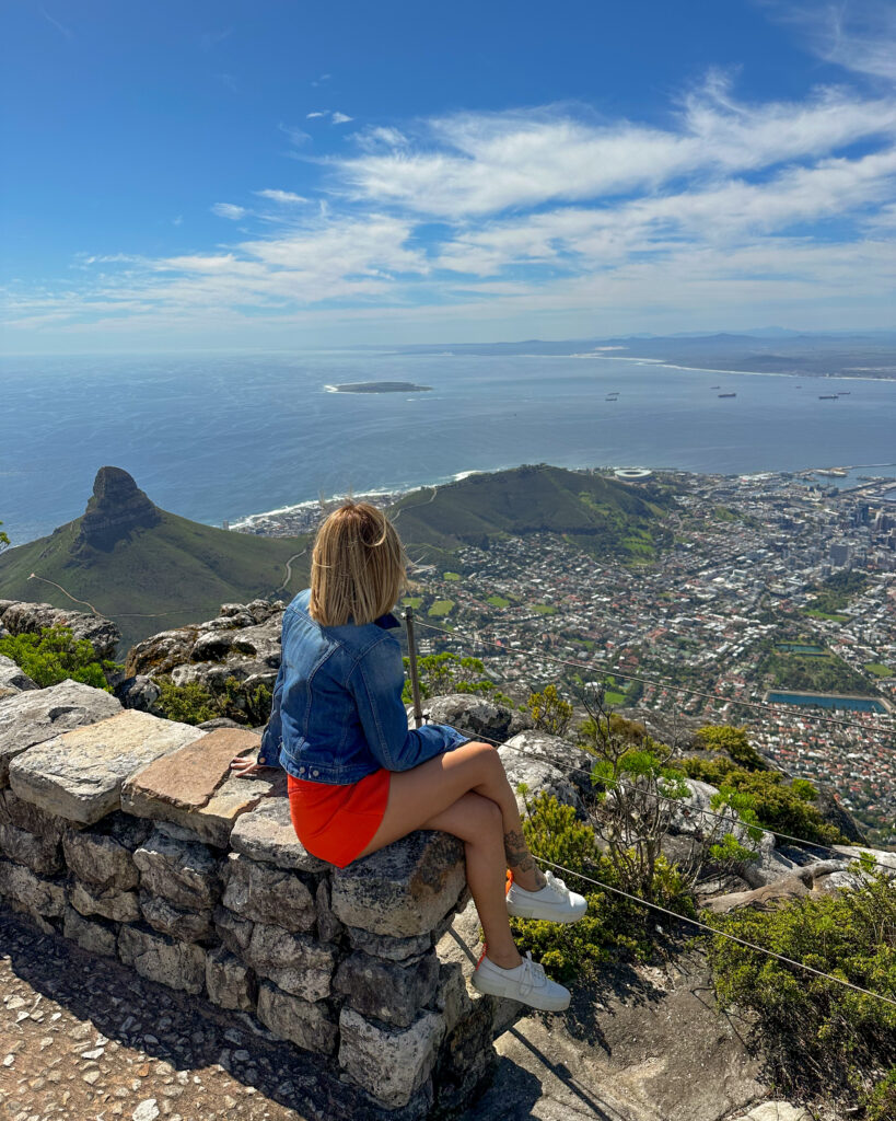 Ragazza seduta opra una roccia in cima alla Table Mountain a Cape Town con vista su tutta la città